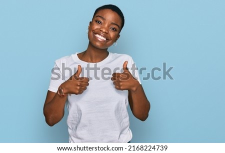 Young african american woman wearing casual white t shirt success sign doing positive gesture with hand, thumbs up smiling and happy. cheerful expression and winner gesture.  Royalty-Free Stock Photo #2168224739