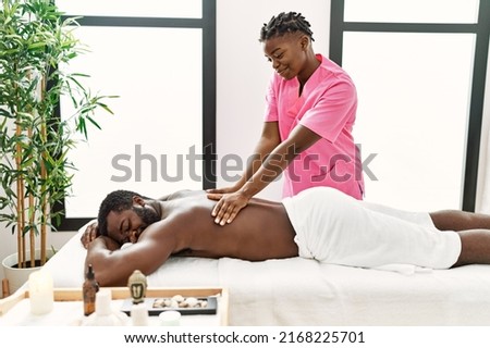 Young physiotherapist woman smiling happy giving back massage to african american man at the clinic. Royalty-Free Stock Photo #2168225701