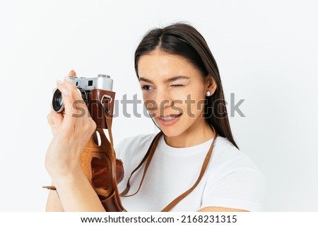 Photographer young woman holding a camera, taking pictures while standing against a white studio backdrop