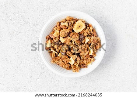 Homemade granola in a white bowl on a white background, overhead view. Homemade whole grain musli with bananas and dark chocolate for breakfast. Top view, light, airy, clean. Breakfast cereal. Royalty-Free Stock Photo #2168244035