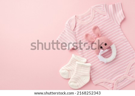 Baby concept. Top view photo of infant clothes pink bodysuit socks and knitted bunny rattle toy on isolated pastel pink background with empty space