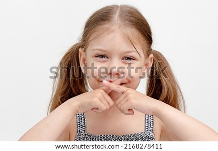 Caucasian smiling little girl of 6 years holding crossed fingers on mouth showing difficulty speaking as results in inability to control the muscles used in speech. Concept dysarthria Royalty-Free Stock Photo #2168278411