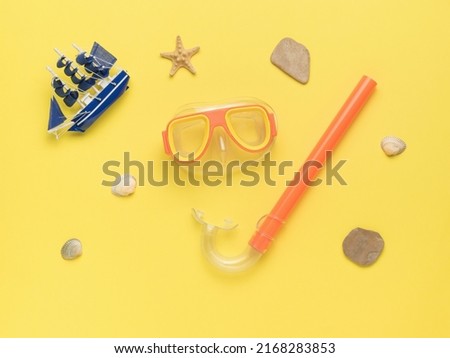 A small boat, a set for swimming and stones on a yellow background. Minimal concept of scuba diving and summer recreation. Flat lay.