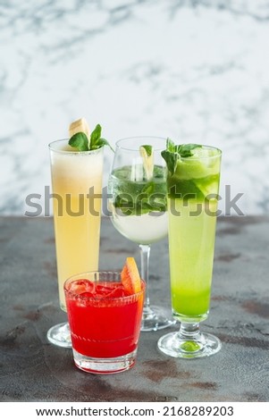 Four summer refreshing cocktails with lemon and mint, vegan beverages on dark marble textured table, heathy lifestyle from the top