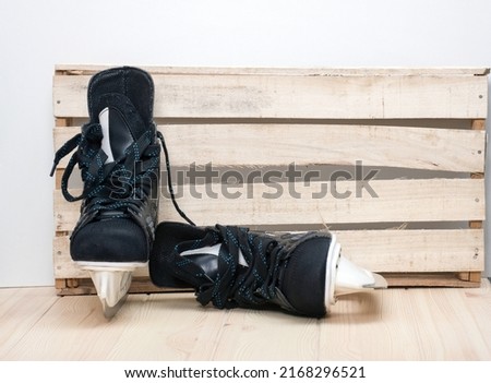 A pair of black hockey skates with well-sharpened metal blades in a white plastic frame designed to play ice hockey stay next to the craft wooden wall waiting for game starts
