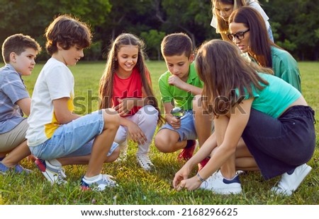 Children having outdoor biology class. Kids learning to take care of nature. Schoolkids, classmates and friends together with teacher sitting on meadow and looking at insects through magnifying glass Royalty-Free Stock Photo #2168296625