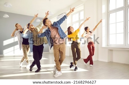 Happy energetic young hip-hop dancers dance together in bright spacious dance studio. Active young women and men in modern casual clothes pursue their hobbies and learn new dance movements together. Royalty-Free Stock Photo #2168296627