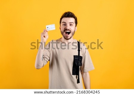 Happy casual man wearing t-shirt posing isolated over yellow background holding credit card with a happy face standing and smiling with big smiles.
