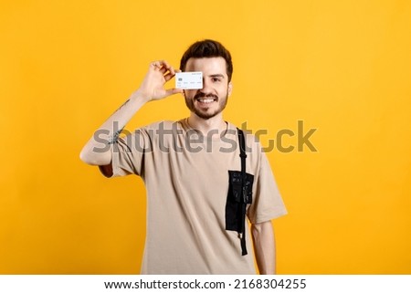 Cheerful caucasian man wearing casual clothes posing isolated over yellow background showing plastic credit card near face. Shopping and finance concept.