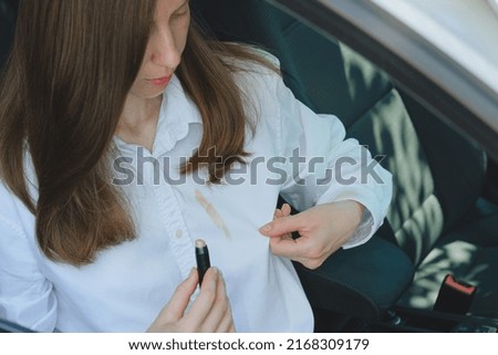 Woman showing a cosmetic stain on a white shirt while sitting in the car. High quality photo