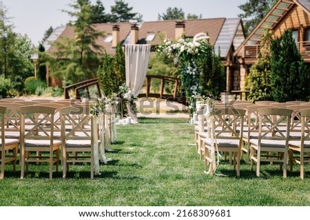 Very beautiful outside ceremony. classical wedding in park. The arch is wooden. White flowers and greenery. Brown chairs. Path from the petals of peony