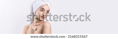 Beautiful girl with thick eyebrows and perfect skin at white background, towel on head, beauty photo. Holds a cosmetic roller.