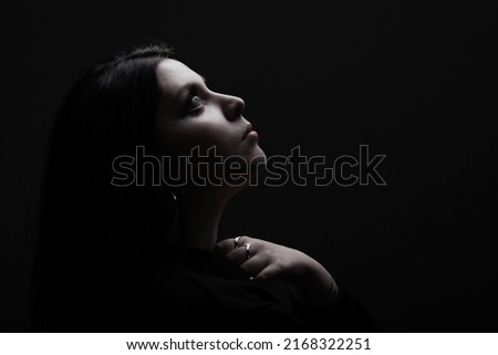 Side lit silhouette portrait of a girl looking up against black background