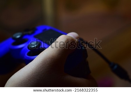 Young boy's hand pressing blue video game console controller.