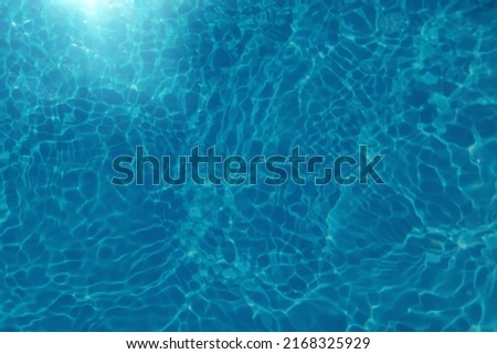 Defocus blurred transparent blue colored clear calm water surface texture with splashes and bubbles. Trendy abstract nature background. Water waves in sunlight. Blue water background.