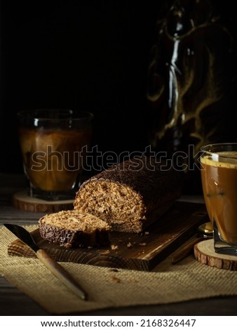 Chocolate cake roll with cut piece on wooden board and coffee. Rustic style, vertical with copy space