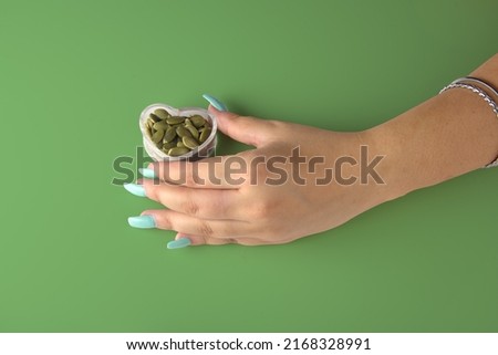 Fashionable spring summer nail art hand holding a bowl of the healthy heart of pumpkin seeds with a seamless grass green color background.