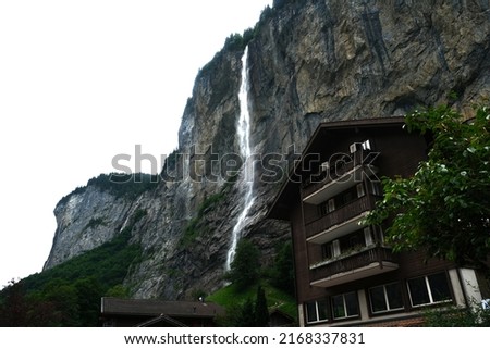 A picture of Lauterbrunnen waterfall with hotel insight. It encompasses the village of Lauterbrunnen, set in a valley featuring rocky cliffs and the roaring, 300m-­high Staubbach Falls.