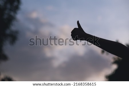 Silhouette of people making and showing thumbs up hand sign with blurred sunset sky background