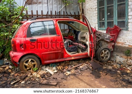 An abandoned and scrapped red hatchback car in the wild