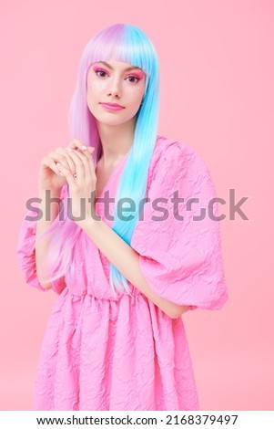 A cute girl with bright makeup and in colored violet-blue wig poses in stylish pink dress. Pink background. Fashion. Hairstyle, hair coloring, make-up. Japanese anime style. 