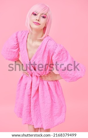 Beauty, fashion. Portrait of a cute teen girl with bright pink makeup and pink hair smiling and posing in fashionable pink dress. Pink background.