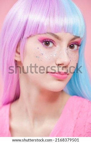 Tender, pretty girl with colored purple-blue hair and bright pink makeup with shiny glitter freckles. Studio portrait on a pink background. Hairstyle, hair coloring. Make-up and cosmetics.