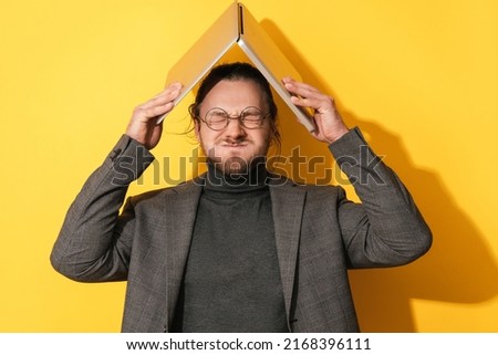 Young man making silly face and holding laptop computer above his head on yellow background Royalty-Free Stock Photo #2168396111