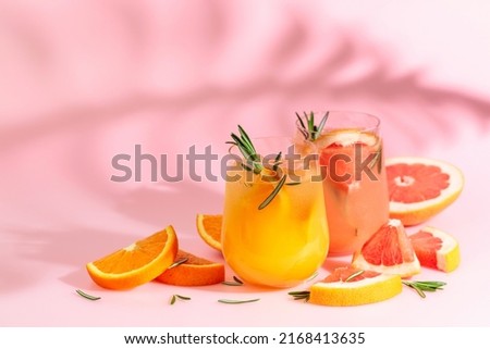Summer cocktails with grapefruit, orange, rosemary, and ice. Drinks on pink background with palm leaf shadow. Summer, tropical, fresh cocktail concept.