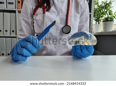 Doctor is holding silicone implant for breast augmentation and scalpel. Plastic surgery to increase size of breast. Professional doctor in field of plastic surgery