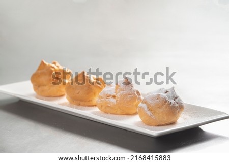Decorating profiteroles with powdered sugar. Eclairs with icing sugar on black background