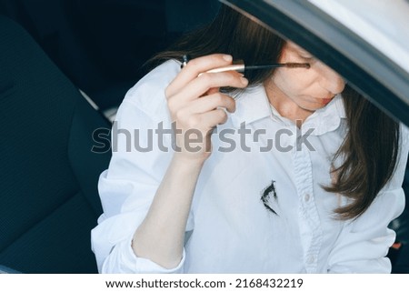 Cosmetic stain on white shirt. Woman applying mascara while sitting in the car. High quality photo
