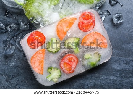Fresh cut vegetables frozen in ice on dark background