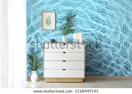 Chest of drawers near wall with print of clear blue water in room