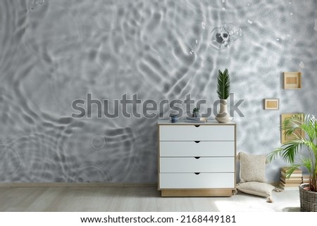 Chest of drawers in room near wall with print of clear water 