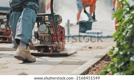 Roadworks Construction Worker Using Ground Plate Compactor Preparing Surface for Laying Sidewalk Pavement Flagstones Royalty-Free Stock Photo #2168451549