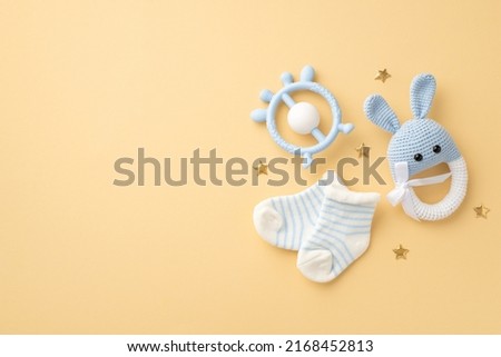 Baby accessories concept. Top view photo of blue teether knitted bunny rattle toy tiny socks and gold stars on isolated pastel beige background with copyspace