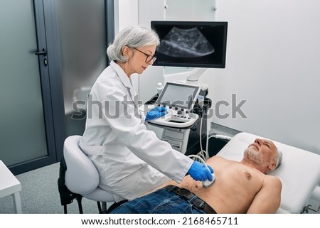 Ultrasound specialist doing ultrasonography of abdominal cavity for mature male patient with ultrasound machine at hospital Royalty-Free Stock Photo #2168465711