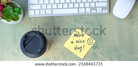 banner with note with words HAVE A NICE DAY with smile and coffee in papper cup, keyboard, cactus and mause on a wooden table. concept of good start to day. top view of the desktop. Flat lay
