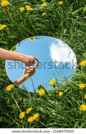 nature concept - hand touching sky reflection in round mirror on summer field Royalty-Free Stock Photo #2168470455