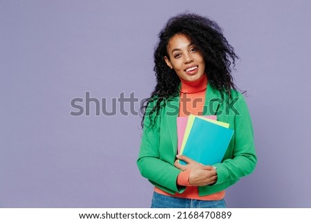 Teacher smiling elegant charismatic young black curly woman 20s wears green shirt looking camera holding in hands coloured textbooks isolated on plain pastel light violet background studio portrait