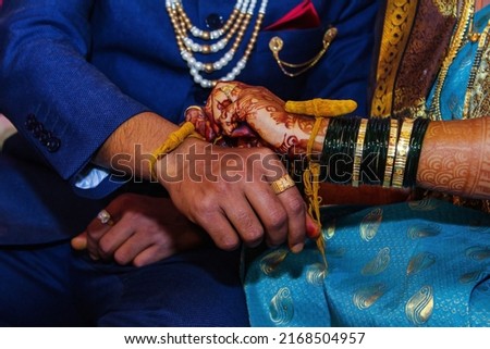 Stock photo of Indian bride and groom wearing beautiful colorful traditional cloths. bride tying raw turmeric band to groom's hand during hindu wedding rituals. Picture captured at India wedding .