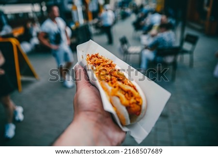 man holds fresh hot dog with sauce in hands. Street food, fast food outdoor Royalty-Free Stock Photo #2168507689