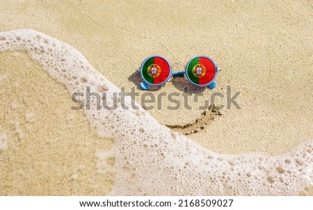 Sunglasses with flag of Portugal on a sandy beach. Nearby is a sea lightning and a painted smile. The concept of a successful vacation in the resorts of the Portugal.