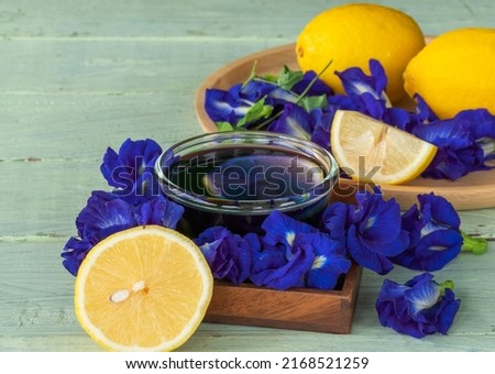 Healthy warm tea made from butterfly pea flowers in glassed bowl, fresh blue pea flowers, and lemons on old wooden background.