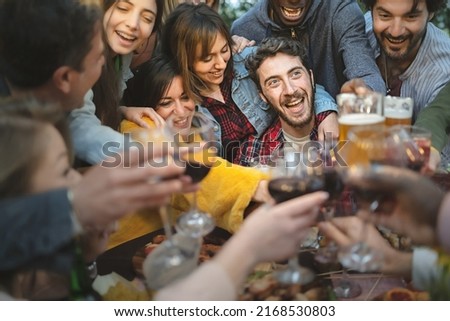 A large group of friends celebrates a birthday by crowding around the birthday boy, clinking glasses of wine and beer amidst hilarity, happiness and laughter - lifestyle
