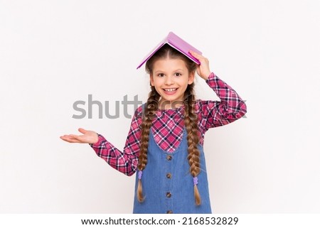 A child with a book on his head smiles broadly on a white isolated background. Reading for schoolchildren.
