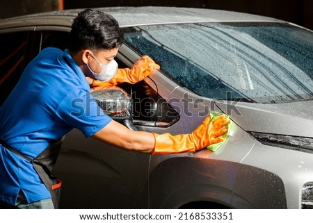 Professional worker with gloves washing and polishing a vehicle with microfiber cloth in professional car wash station.
