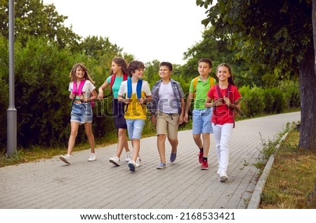 School friendship. Funny schoolchildren group with backpacks have fun walking together on path in park. Cheerful boys and girls in summer casual clothes return home from school lessons together. Royalty-Free Stock Photo #2168533421