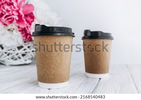 Coffee paper cup on white background with peony flowers. Take away coffee cup, mockup.